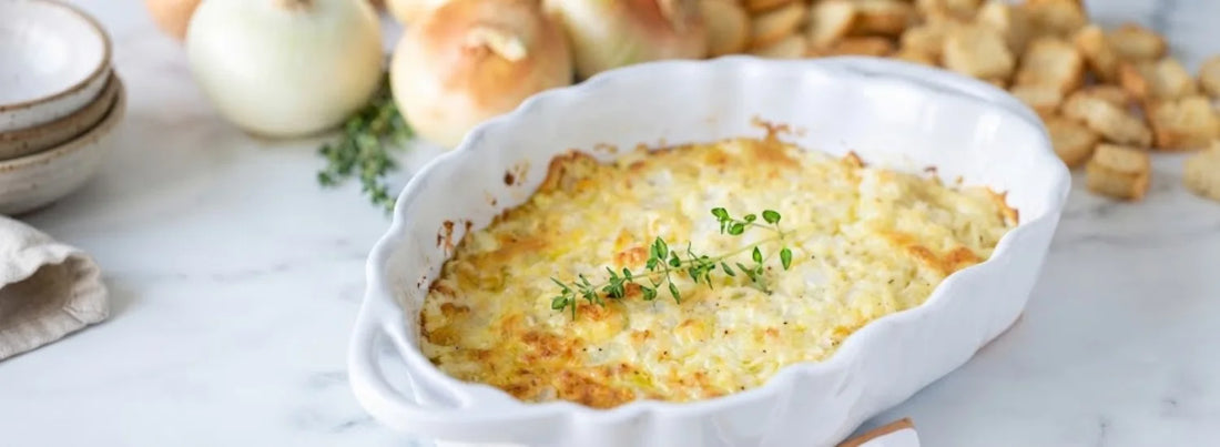 A yellow-white dish of Vidalia onion dip, crusted with toasted cheese on top and garnished with an herb. Image sourced from Pizzazzerie’s Baked Vidalia Onion Dip recipe.