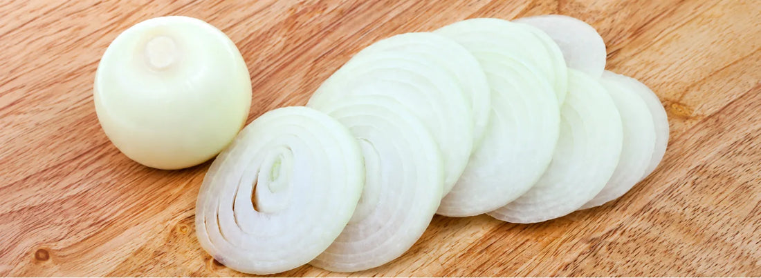White onion slices and a peeled white onion bulb arranged on a wooden board.