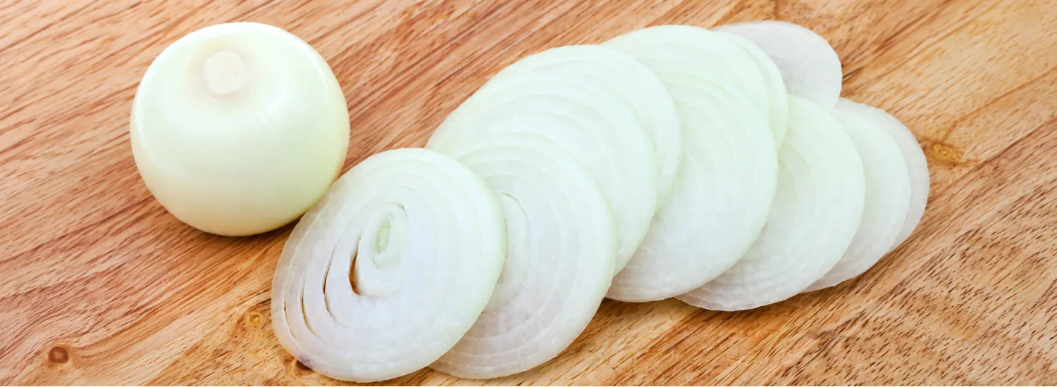 White onion slices and a peeled white onion bulb arranged on a wooden board.