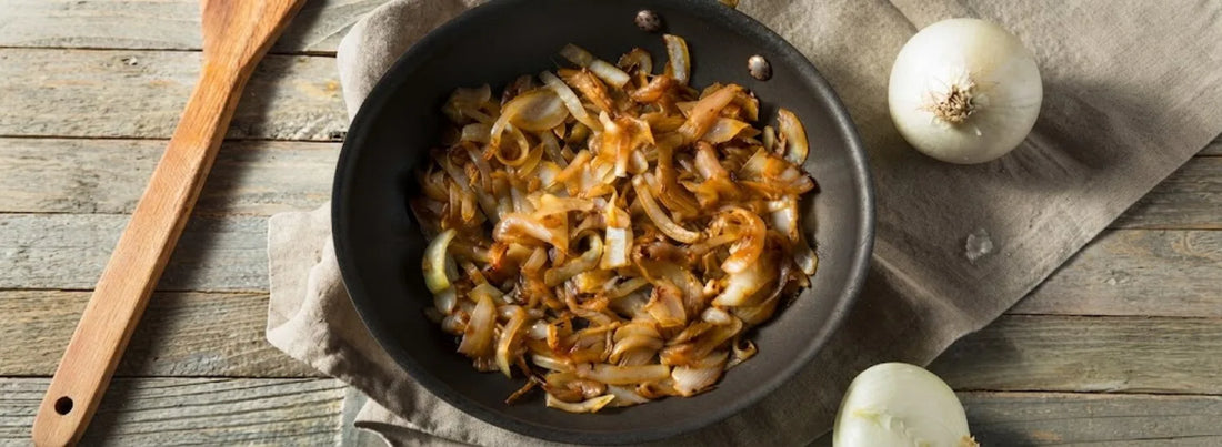 A top-down view of a frying pan in which onion strips are caramelizing.