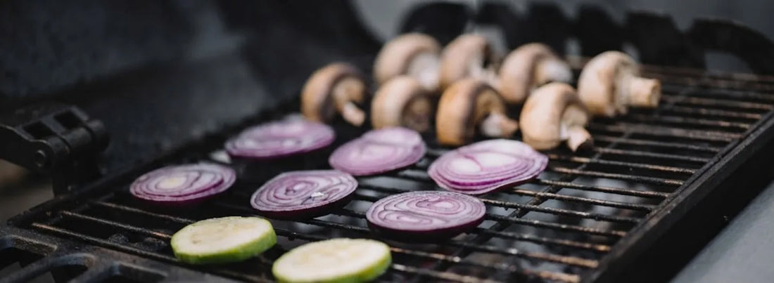 Sliced red onions on a grilltop, alongside slices of halved mushrooms and cucumbers.