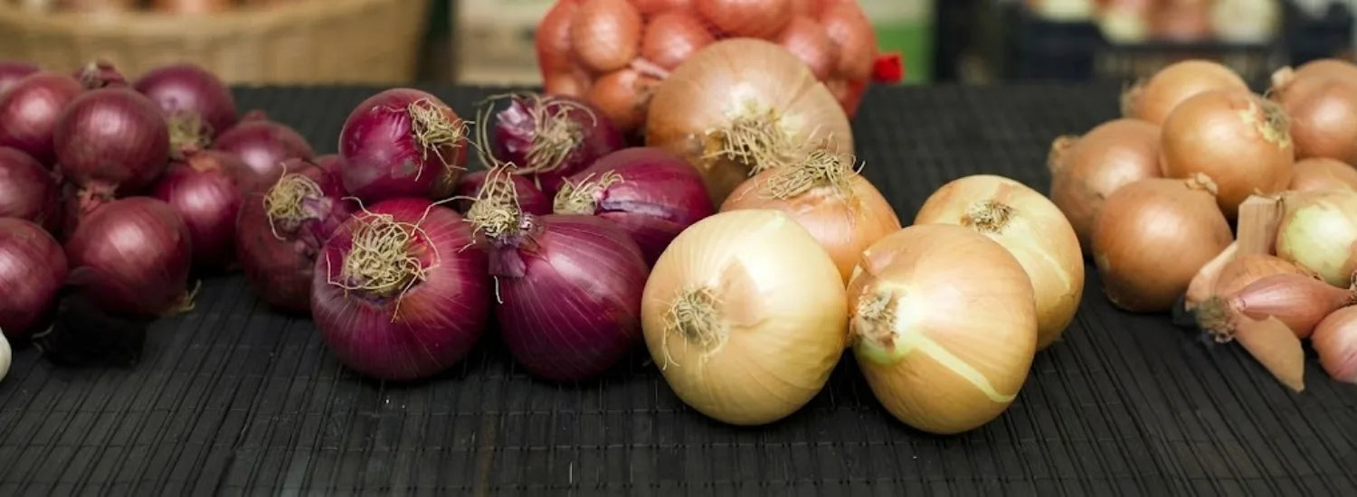 A variety of yellow and red onions piled up next to one another.