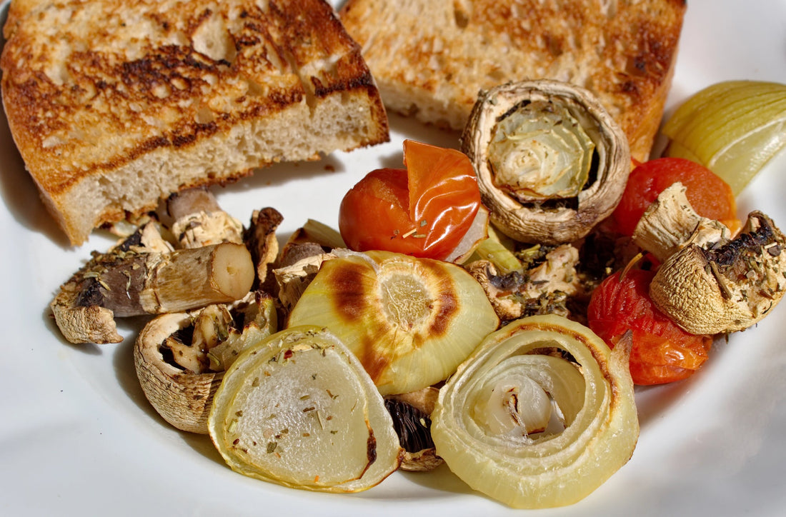 A closeup of roasted onions on a plate next to roasted tomatoes and toast.