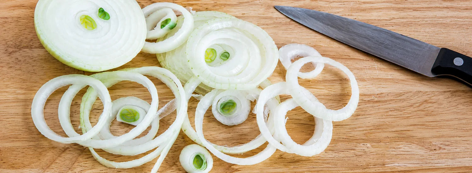 Many onion rings on a wooden cutting board, next to a knife.
